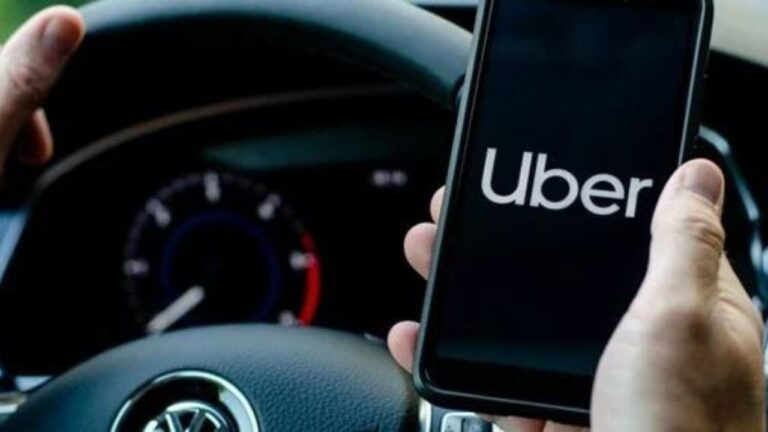 Um motorista segurando o volante e outra mão na celular com o símbolo da Uber